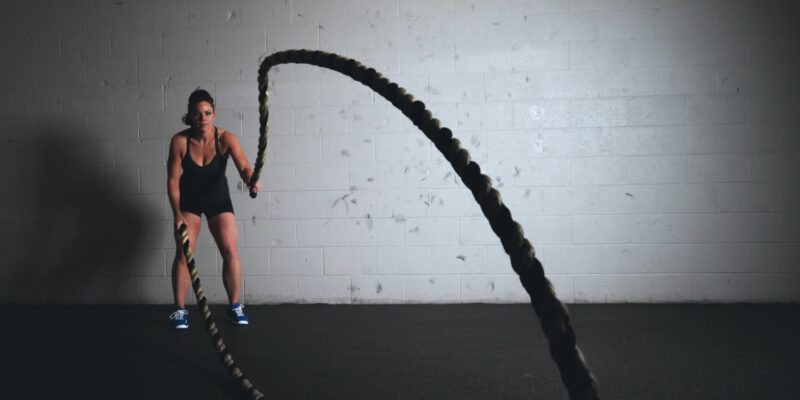 The 7 Proven HIIT Benefits blog featuring a woman in the gym swinging two ropes